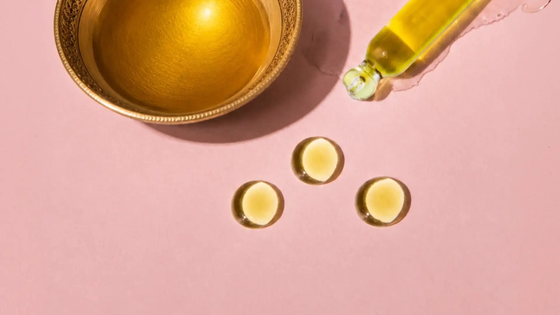 Three golden Kesaradi drops beside a gold Ayurvedic bowl and dropper